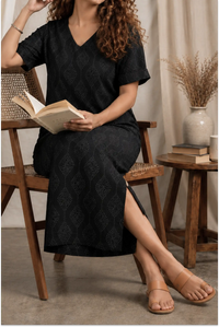 Woman in a black dress sitting on a wooden chair reading a book in a cozy room.