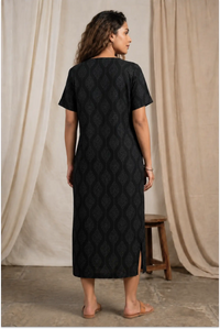 Woman wearing a black quilted dress standing against a neutral curtain backdrop