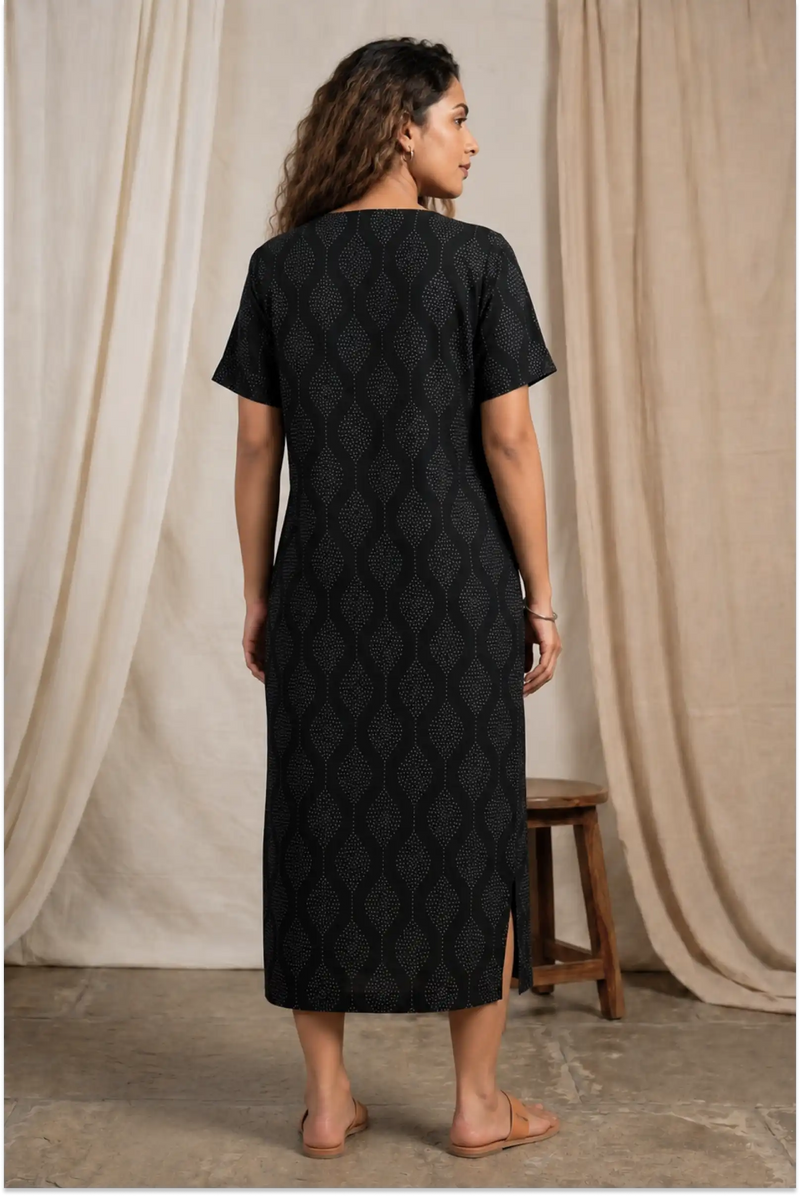 Woman wearing a black quilted dress standing against a neutral curtain backdrop