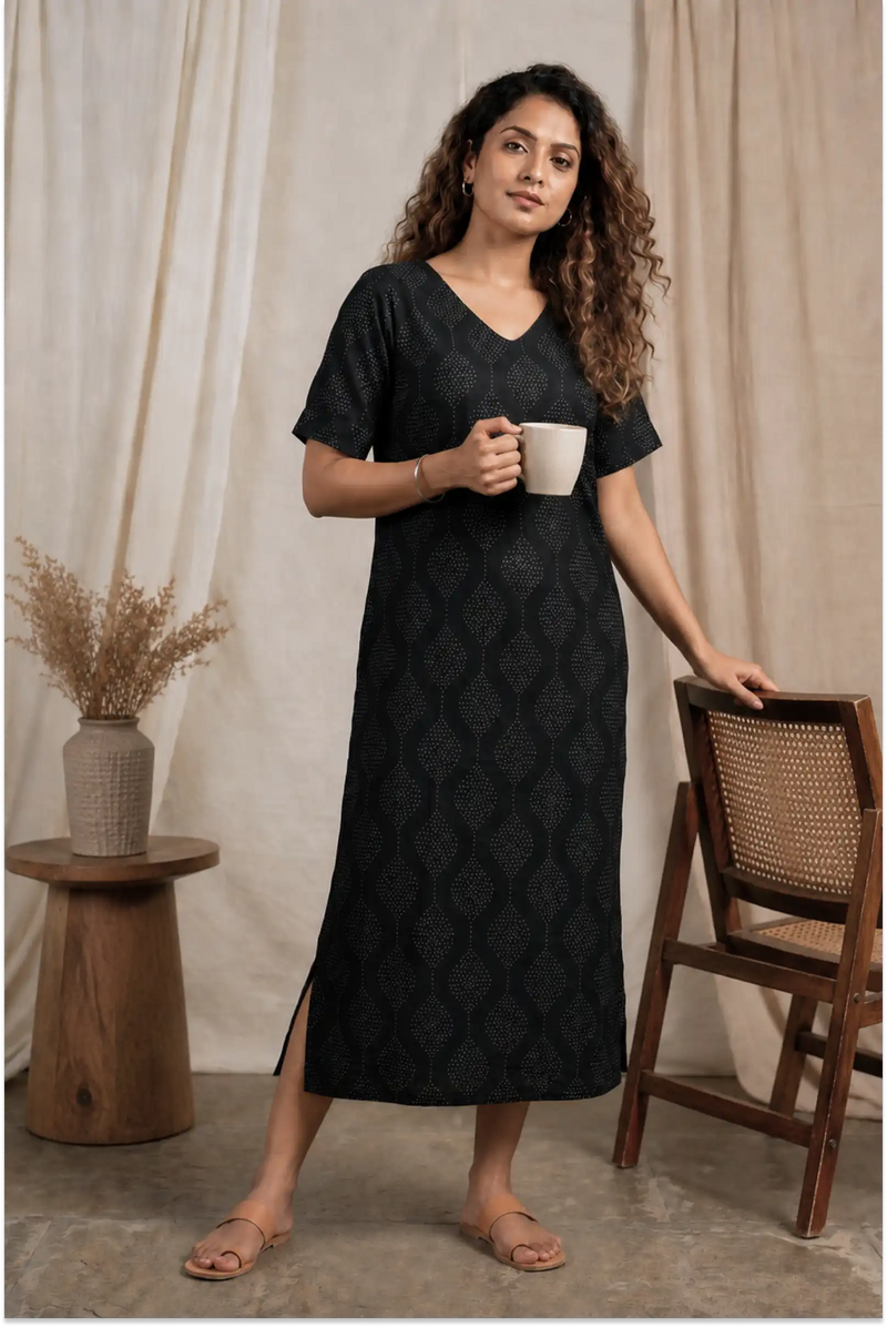 Woman in a black patterned dress holding a white mug in a home setting.